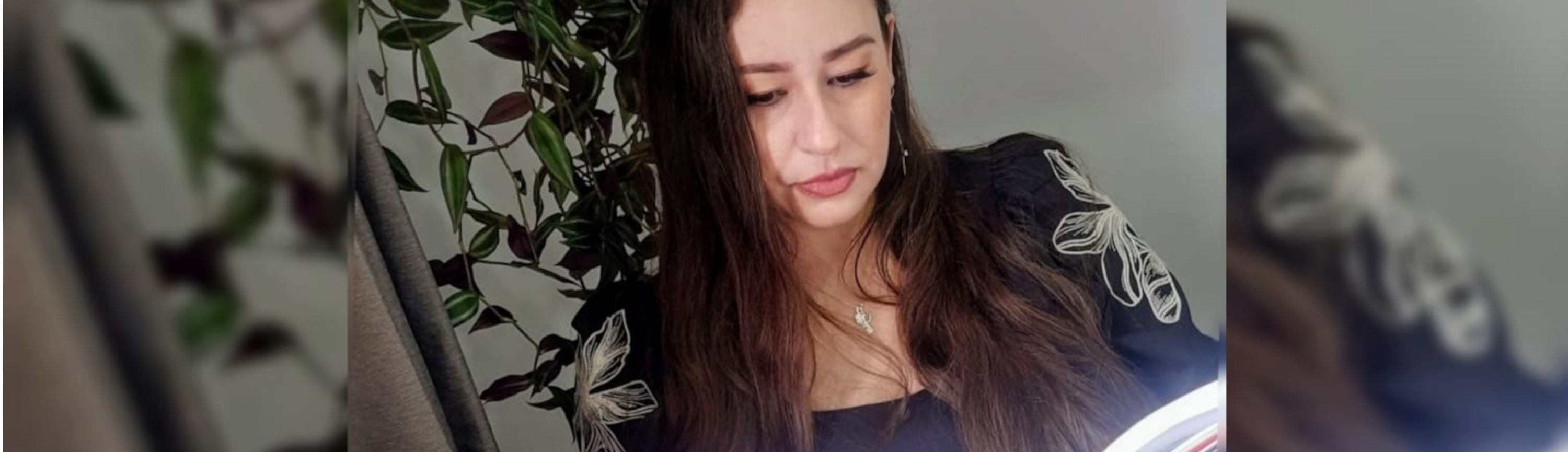 Psicóloga Fernanda com expressão séria, lendo um livro com planta ao fundo