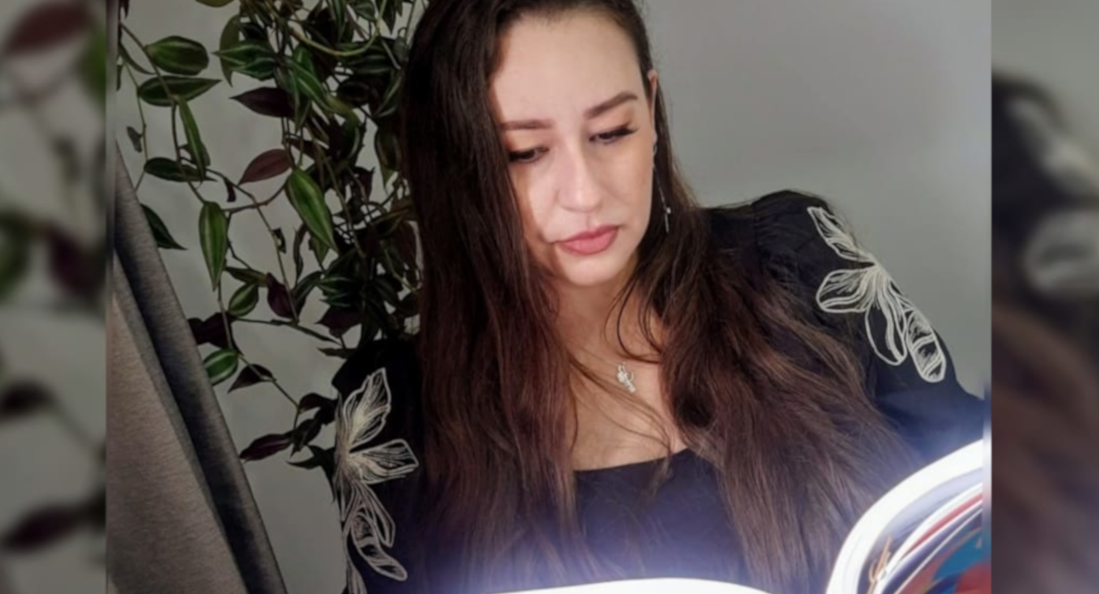 Psicóloga Fernanda com expressão séria, lendo um livro com planta ao fundo